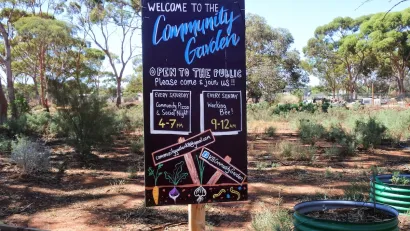 Chalkboard sign at front of a community garden with hours and information.